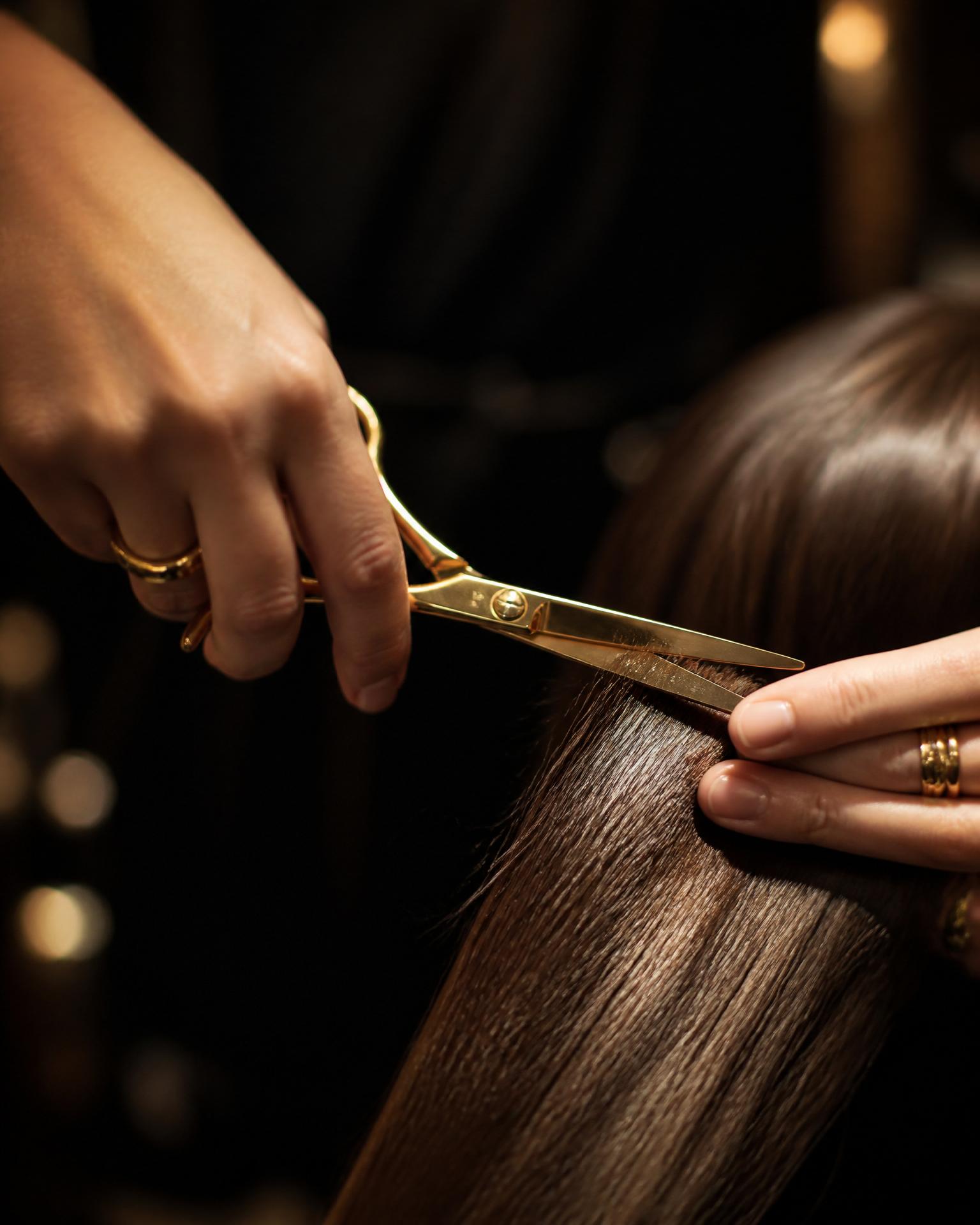 Stylist knipt glanzend bruin haar met gouden schaar — vakwerk bij Yensi Style